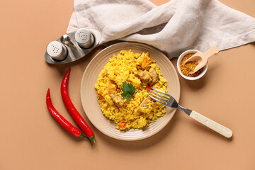 Plate of tasty pilaf with chili peppers and bowl of spices on brown background