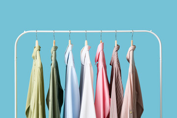 Rack with stylish collar shirts on blue background