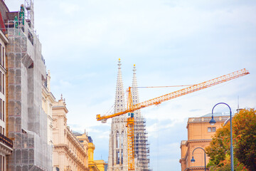 Vienna Votivkirche, a neo-Gothic church with twin spires, under construction with a yellow crane...