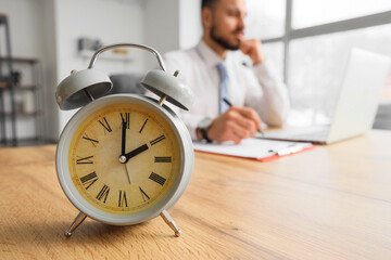 Vintage alarm clock on table against businessman working in office, closeup