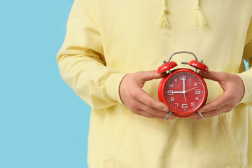 Man with red alarm clock on blue background, closeup