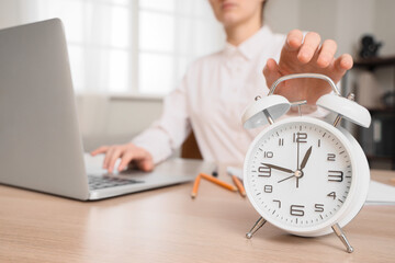 Businesswoman with laptop turning off alarm clock at table in office, closeup