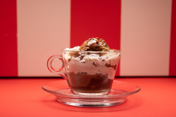 Layered chocolate dessert served in glass cup over red stripes.