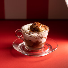 Layered chocolate dessert served in glass cup over red stripes.