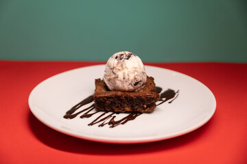 Brownie topped with ice cream scoop and chocolate drizzle, plated.