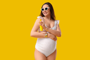 Young pregnant woman applying sunscreen cream on yellow background. Traveling concept