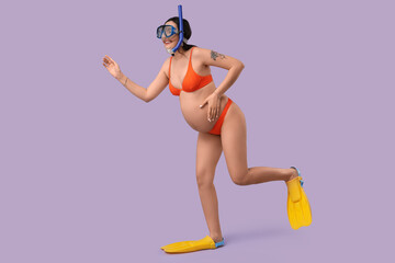 Young pregnant woman in swimsuit with flippers and swimming mask running on lilac background....