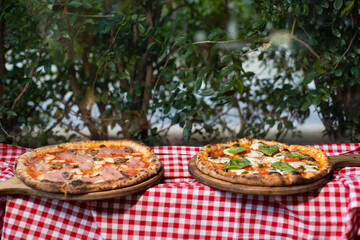 Two freshly baked pizzas on wooden trays with checkered tablecloth.