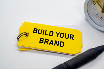 Build your brand message displayed on yellow sticky note held by a hand with pen beside.