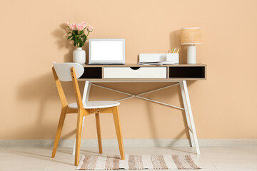 Stylish workspace with modern laptop and beautiful flowers near beige wall