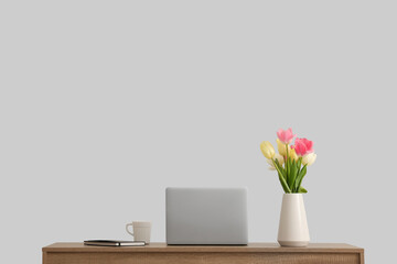 Stylish workspace with modern laptop and beautiful flowers near white wall