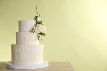 Delicious wedding cake decorated with flowers on wooden table against light green background. Space for text