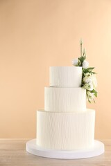 Delicious wedding cake decorated with flowers on wooden table against beige background