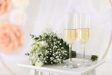 Glasses of champagne and wedding bouquet on table indoors, closeup