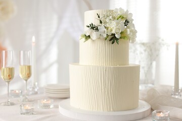 Delicious wedding cake with floral decor and glasses of champagne on table indoors