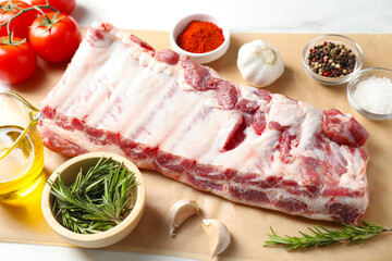 Raw pork ribs, spices and tomatoes on white table, closeup