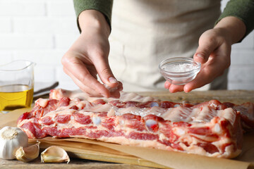 Woman putting sea salt onto raw pork ribs at table, closeup