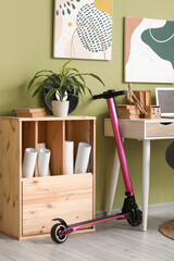 Interior of living room with electric scooter, commode and laptop on workplace near green wall