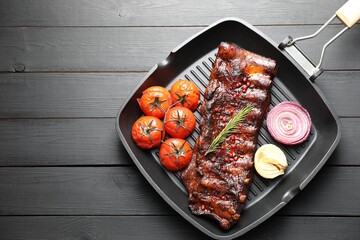 Delicious roasted pork ribs with rosemary, tomatoes and onions on grey wooden table, top view. Space for text