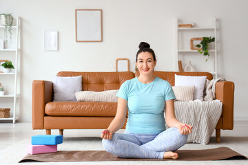 Fototapeta premium Sporty pregnant woman meditating on yoga mat at home