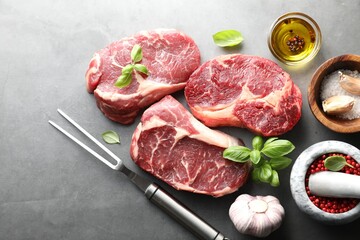 Pieces of raw beef meat, spices and carving fork on grey table, flat lay
