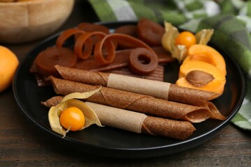 Tasty fruit leather, physalis and apricots on wooden table, closeup