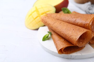 Delicious fruit leather rolls, mint and mango on white table, closeup. Space for text