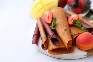 Delicious fruit leather rolls, mint, mango and berries on light table, closeup. Space for text