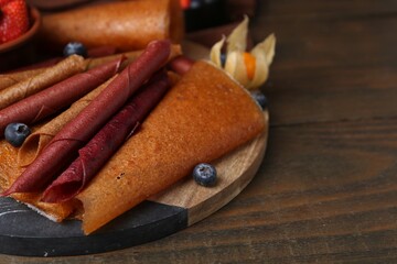 Delicious fruit leather rolls and berries on wooden table, closeup. Space for text