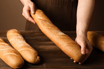 Man with fresh baguettes on brown background