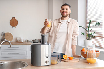 Young man with fresh orange juice and modern juicer in kitchen