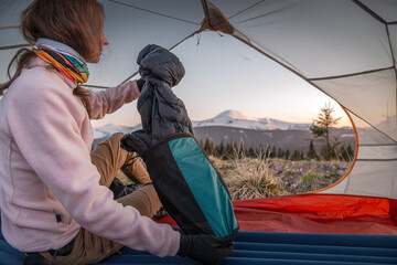 Young female hiker unpacking a sleeping bag from a compression sack in her tent at sunset in the...