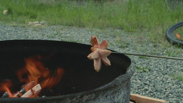 Ein Cervelat brutzelt &uuml;ber dem offenen Feuer, eingeritzt und aufgespie&szlig;t &ndash; der Rauch steigt auf, es duftet nach Holz und R&ouml;staromen. Ein echter Schweizer Grillmoment in der Natur.