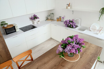 Interior of light kitchen with table, counters and lilac flowers
