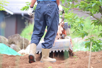 耕運機で畑を耕す農家のおじさん