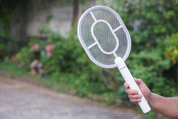 White electric mosquito swatter held firmly in hand, ready to zap away annoying insects in outdoor...