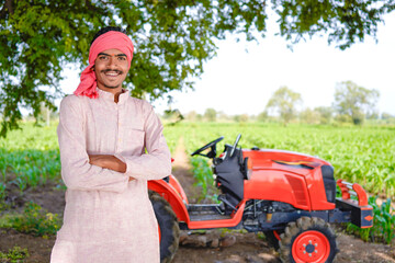 Happy young indian farmer standing with new tractor at agriculture field
