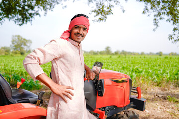 Happy young indian farmer standing with new tractor at agriculture field