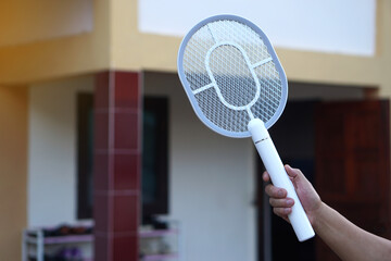 White electric mosquito swatter held firmly in hand, ready to zap away annoying insects in outdoor...