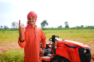 Young indian farmer showing voting sign with finger while standing at agriculture field.