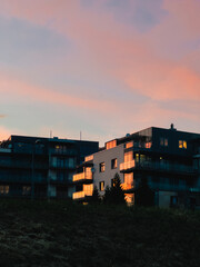 Urban apartments glowing with warm sunset hues, balconies and windows capturing evening light, reflecting tranquil residential landscape against soft twilight sky. buildings reflecting warm colors
