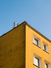 Low angle view capturing a vibrant yellow building corner adorned with antennas on the rooftop, set against a clear blue sky, enhancing telecommunication services in the urban landscape. yellow, blue