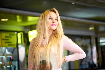 A blonde in a pink sweater and blue jeans poses for a photo. She smiles and she is happy. She has a beautiful figure.