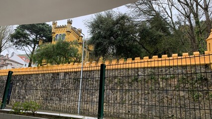 Yellow castle behind iron fence in overcast weather, European heritage site travel, history...