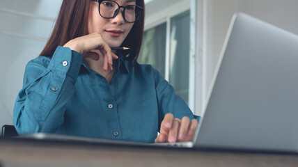 Young asian business woman working on laptop computer at office. Female student using laptop watching online webinar or training web course, looking at computer