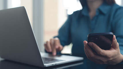 Businesswoman working on laptop computer and using mobile phone at office. Asian woman using smartphone searching the information, surfing the internet with laptop on office table, internet technology