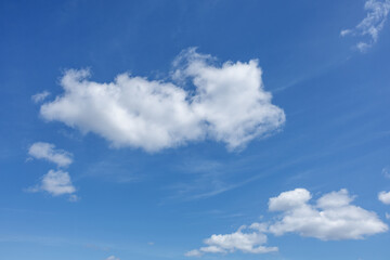 Large white fluffy clouds drift across foreground of bright blue sky, creating serene and peaceful atmosphere. Wispy background cloud trails add gentle textures to the otherwise clear expanse above.