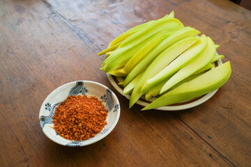 fresh sliced green mango with spicy chily salt under wooden table, traditional asian snack