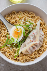 Bowl of ramen served with steamed dumpling, boiled egg and spring onion, vertical shot, close-up