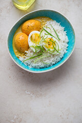 Basmati rice with curried chicken eggs on a light-beige stone background, vertical shot with space, high angle view